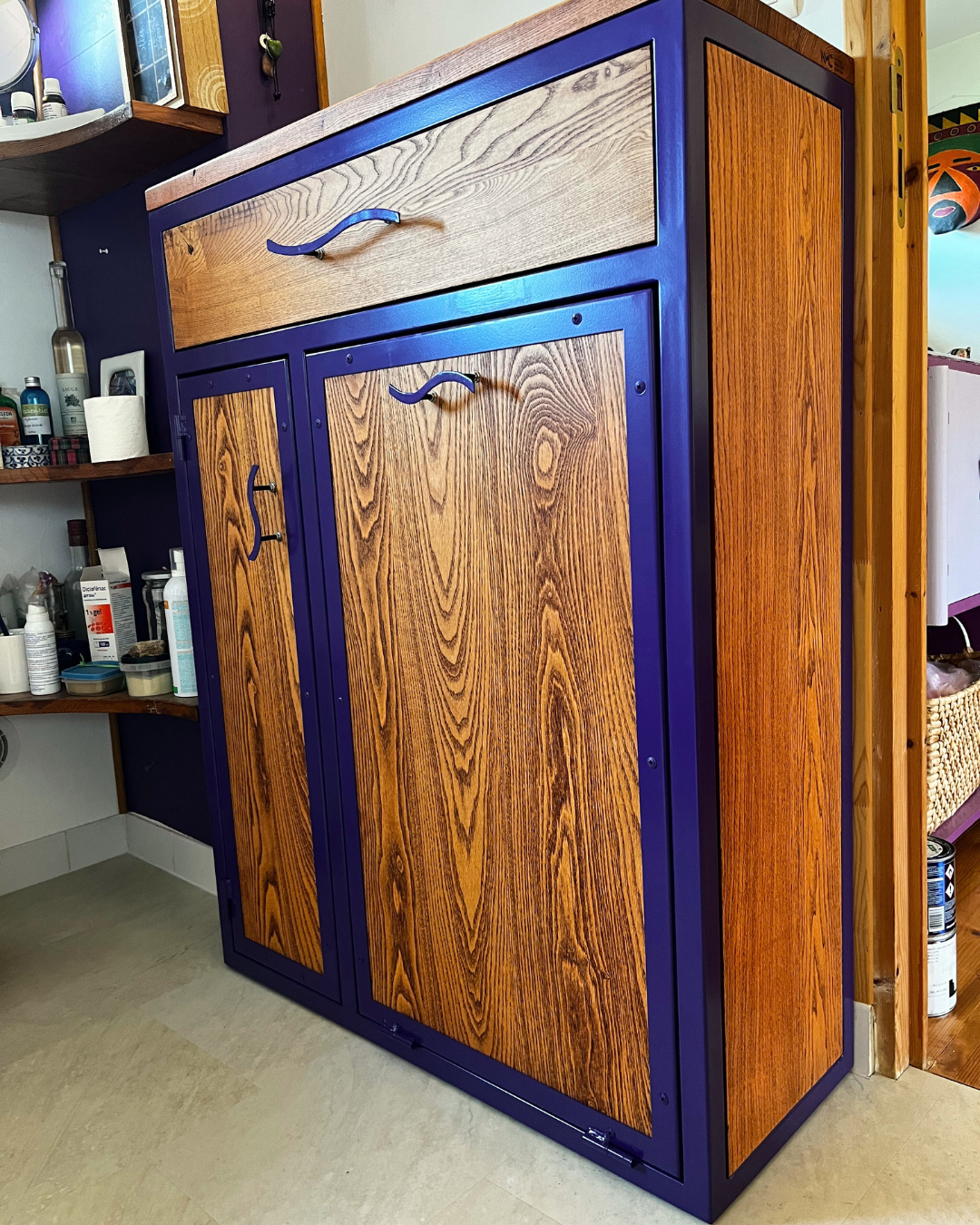 Meuble de rangement personnalisé en frêne massif et structure métallique peinte en violet. Panier à linge intégrée sur porte basculante.