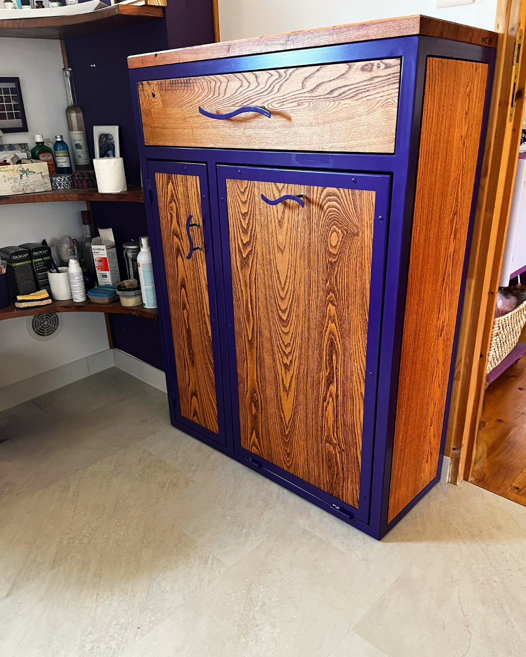 Meuble de rangement personnalisé en frêne massif et structure métallique peinte en violet. Panier à linge intégrée sur porte basculante.